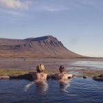 Happy couple in love bathing and relaxing in hot pool with spectacular view of wild landscape