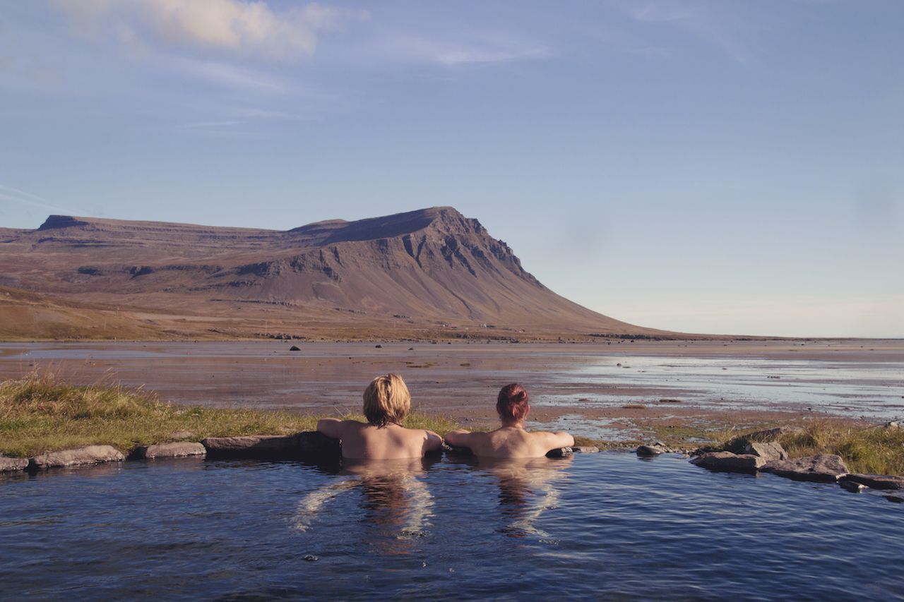 Happy couple in love bathing and relaxing in hot pool with spectacular view of wild landscape