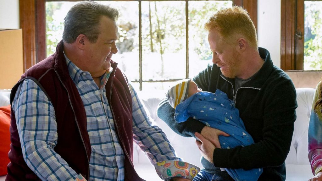 Gay married couple holding a newly adopted child, scene from Modern Family TV series